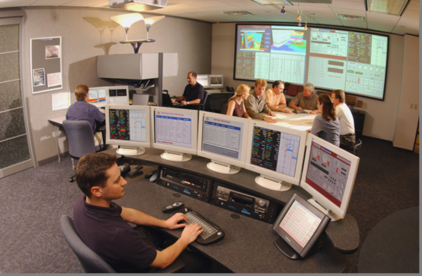 A team in a room looking at computer monitors and meeting over a conference table.